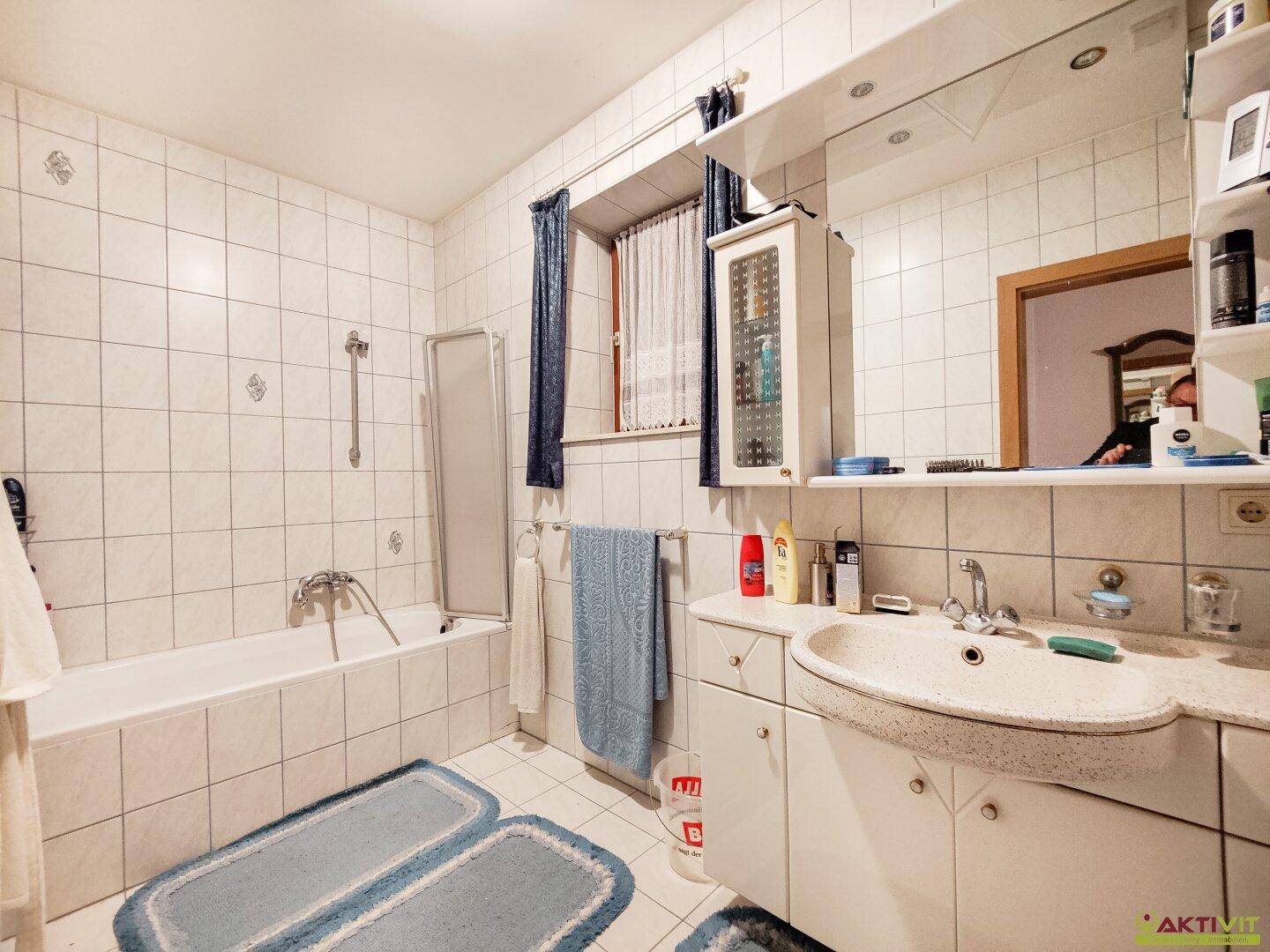 Badezimmer mit Badewanne, Waschbecken und Spiegelschrank, komplett gefliest.