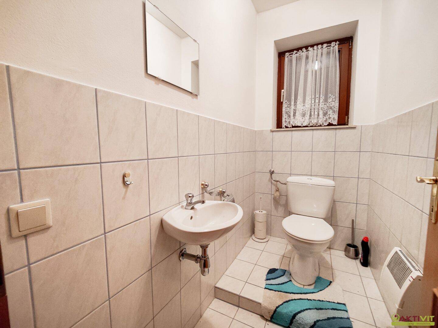 Separate Toilette mit Waschbecken, Fenster und halbhoher Fliesenvertäfelung.