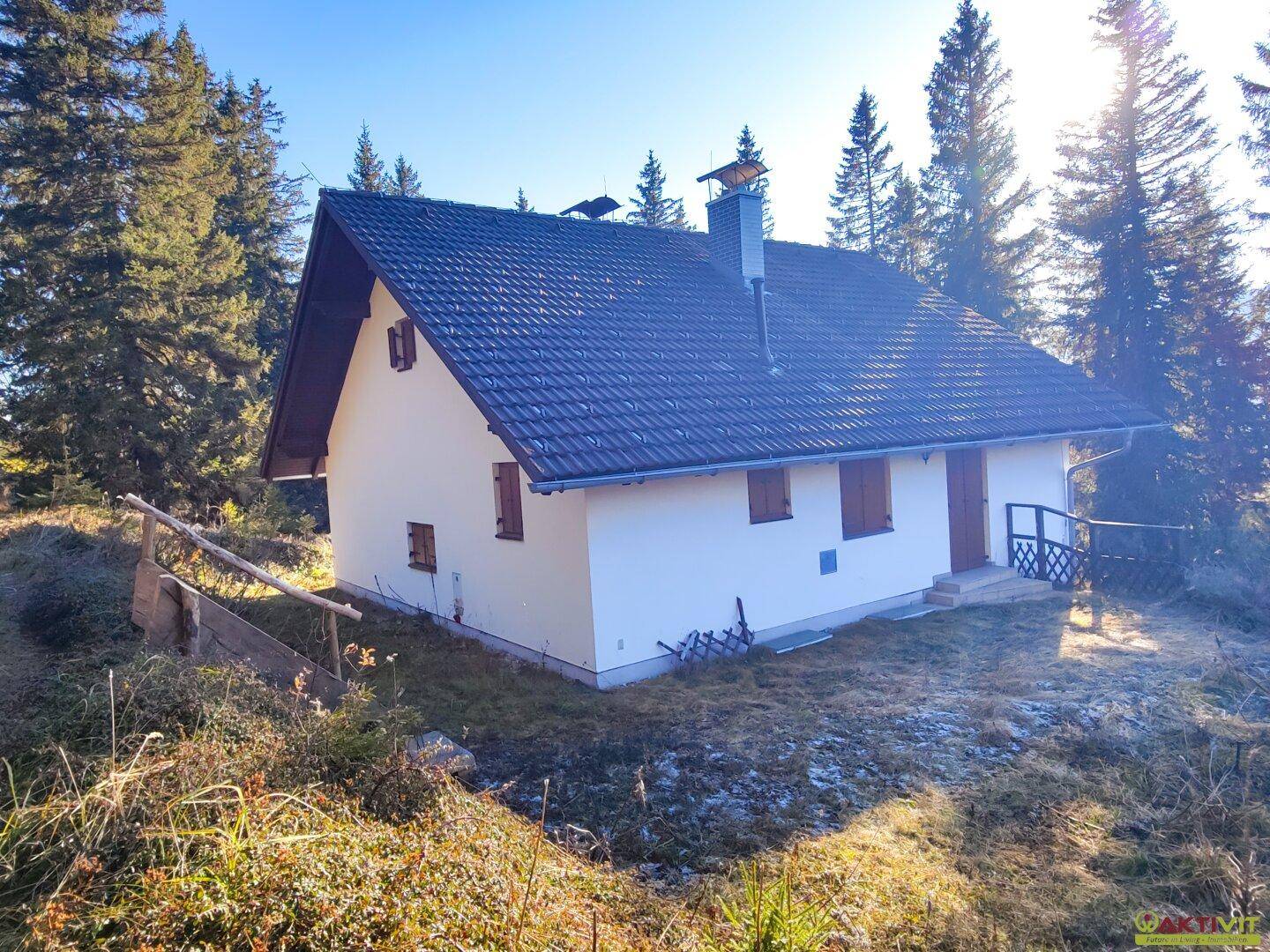Freistehendes Haus mit Satteldach und weißer Fassade, umgeben von Nadelbäumen in ländlicher Umgebung.