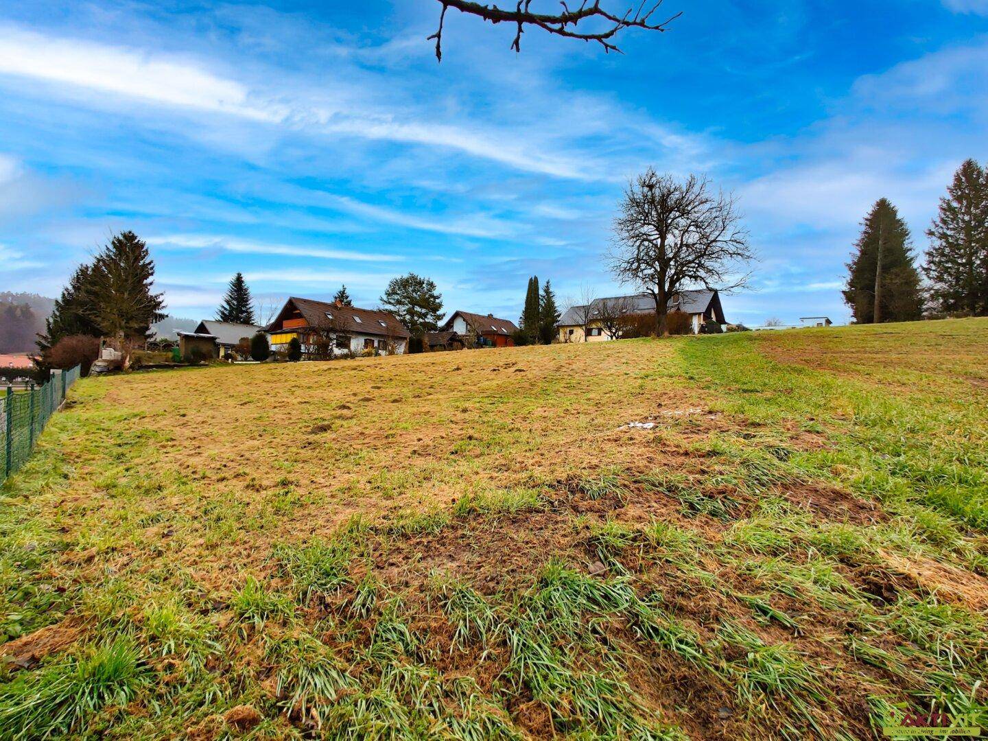 Offenes Feld mit mehreren Wohnhäusern im Hintergrund und weitem Blick in die Landschaft.