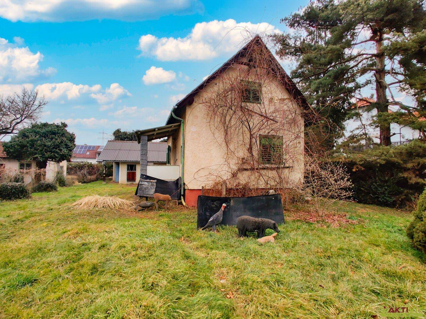 Seitenansicht eines älteren Hauses mit verputzter Fassade und umgebender Grünfläche.