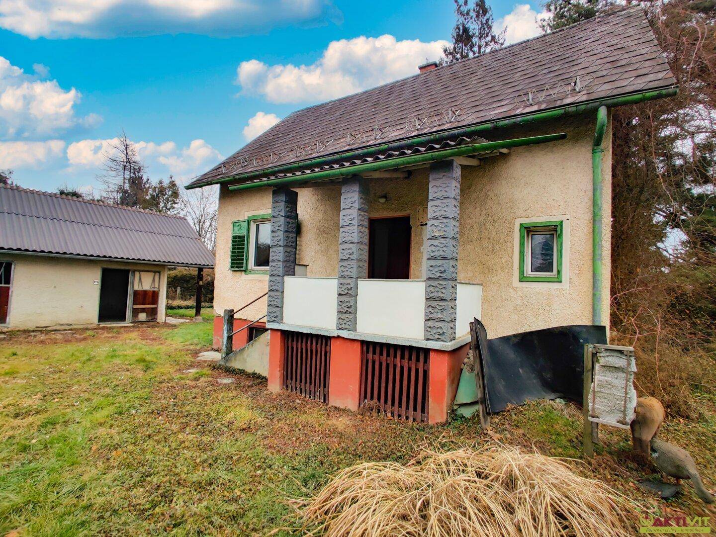 Vorderansicht eines älteren Hauses mit überdachtem Eingangsbereich und grünen Fensterläden.