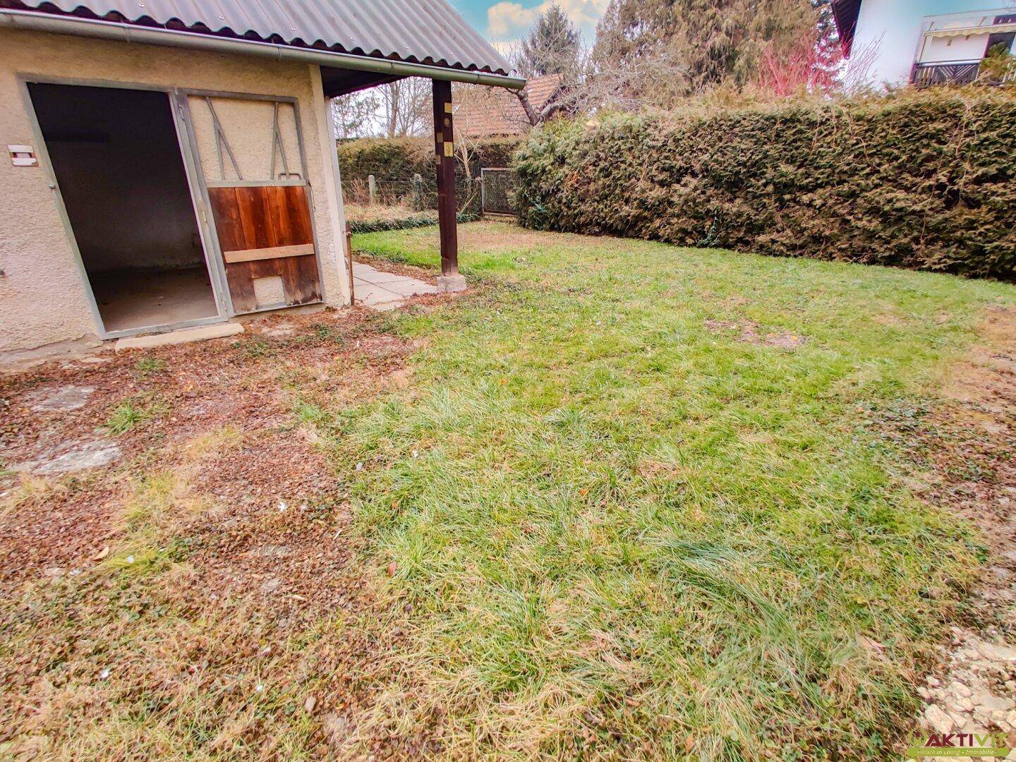 Kleines Nebengebäude mit Holztür und angrenzender Rasenfläche, umgeben von einer Hecke.