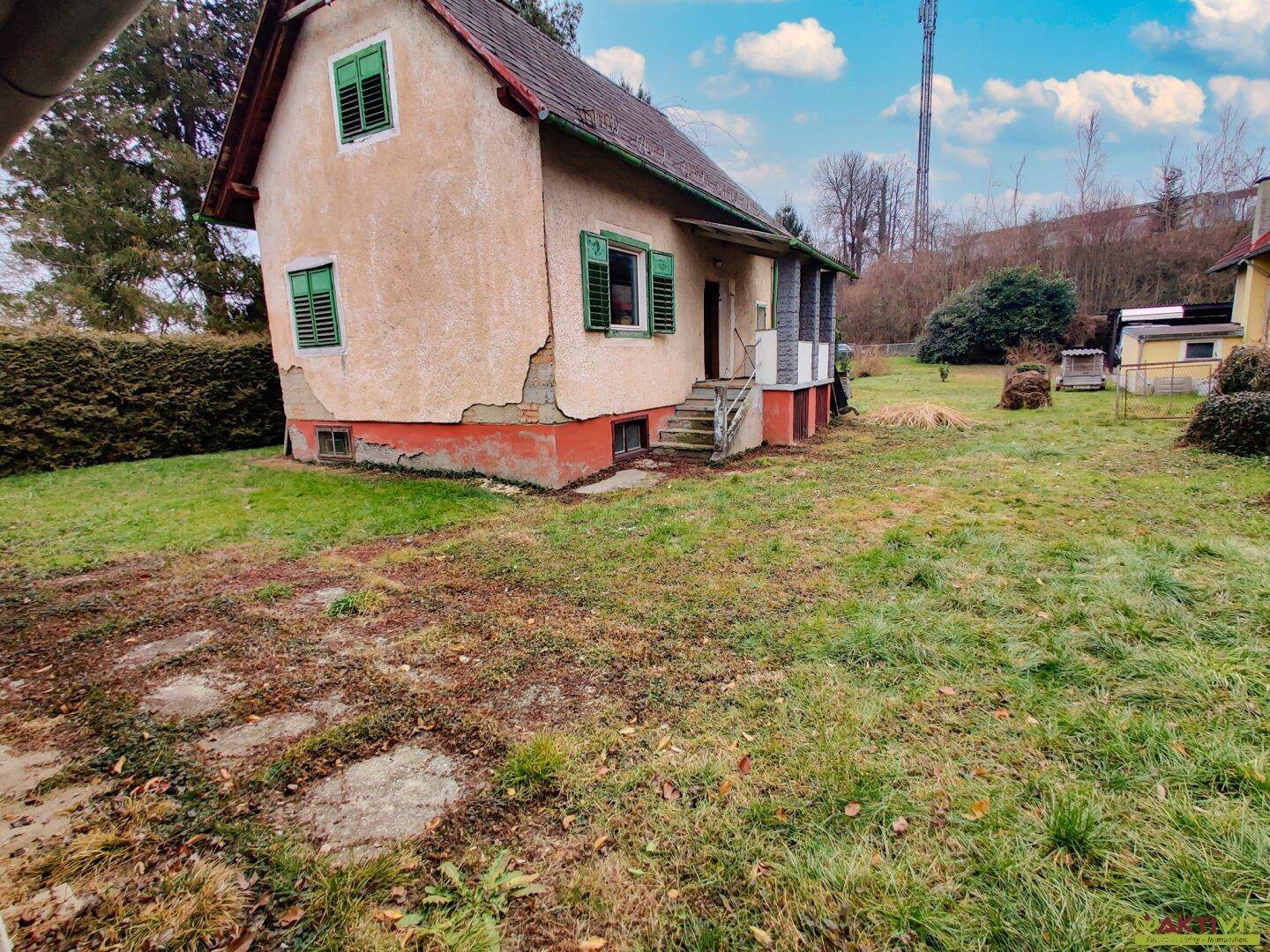 Rückansicht des Hauses mit abblätterndem Putz und Treppenzugang zum Gartenbereich.