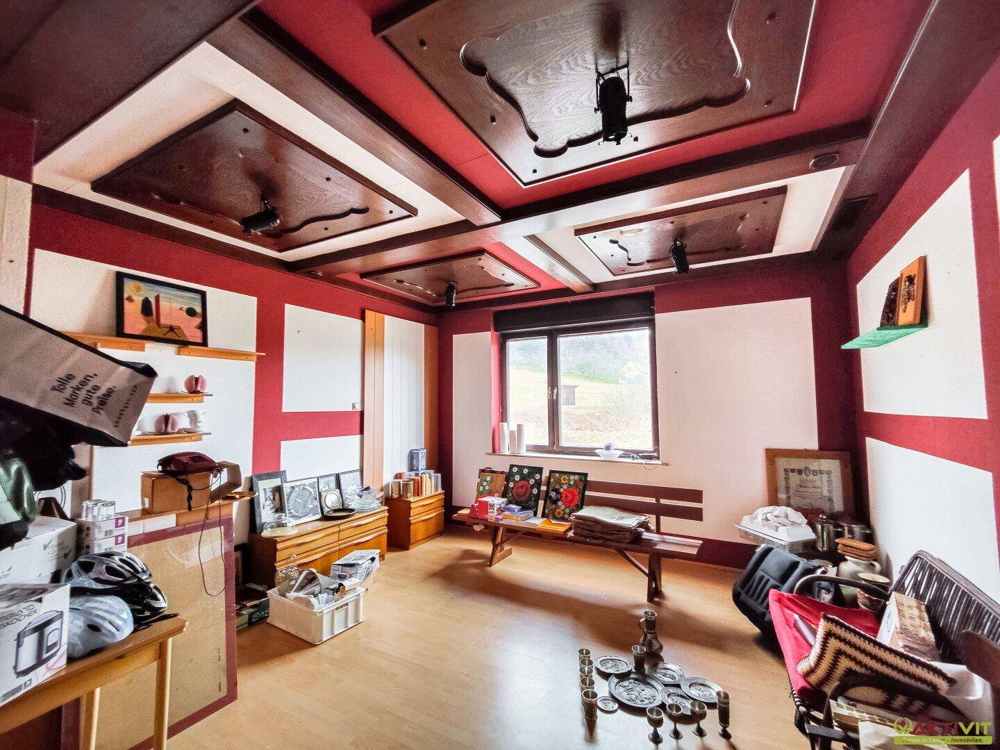 Wohnraum mit roter Wandfarbe, Holzbalkendecke und Blick ins Grüne.