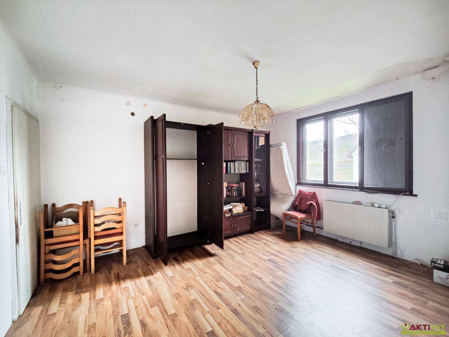 Geräumiger Wohnraum mit Holzfußboden, großem Fenster und Schrank.