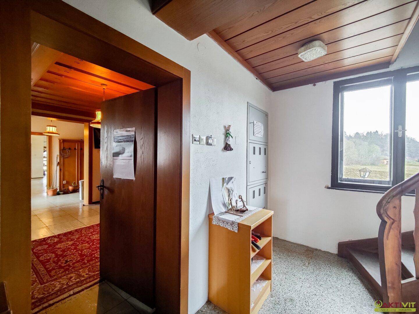 Treppenhaus mit Holztreppe, Fenster und Blick auf die Landschaft.