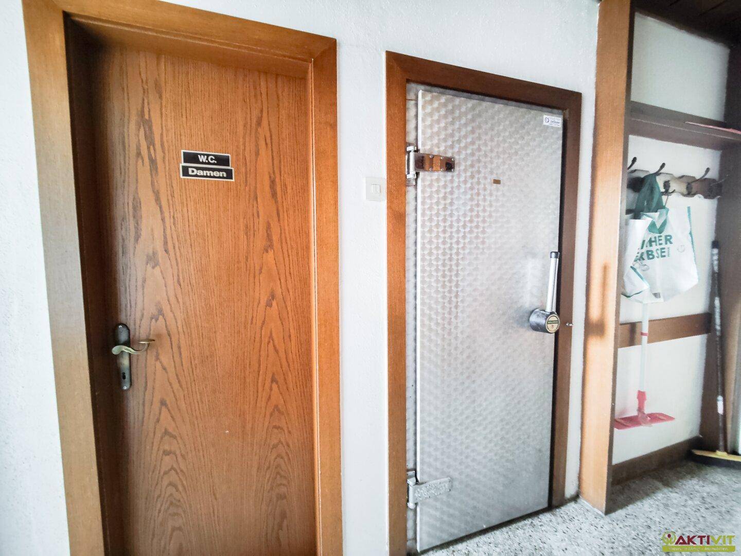 Flur mit Holztüren, darunter eine Tür zum Damen-WC und eine Stahltür.