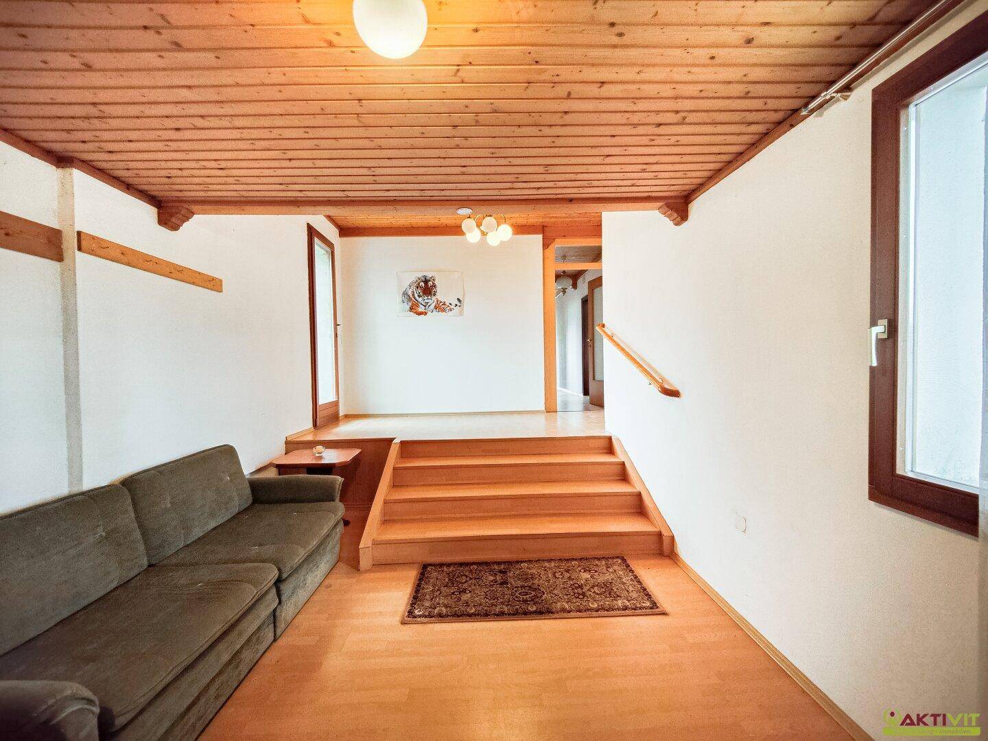 Offener Wohnbereich mit Holzdecke, Stufen und gemütlichem Sofa.