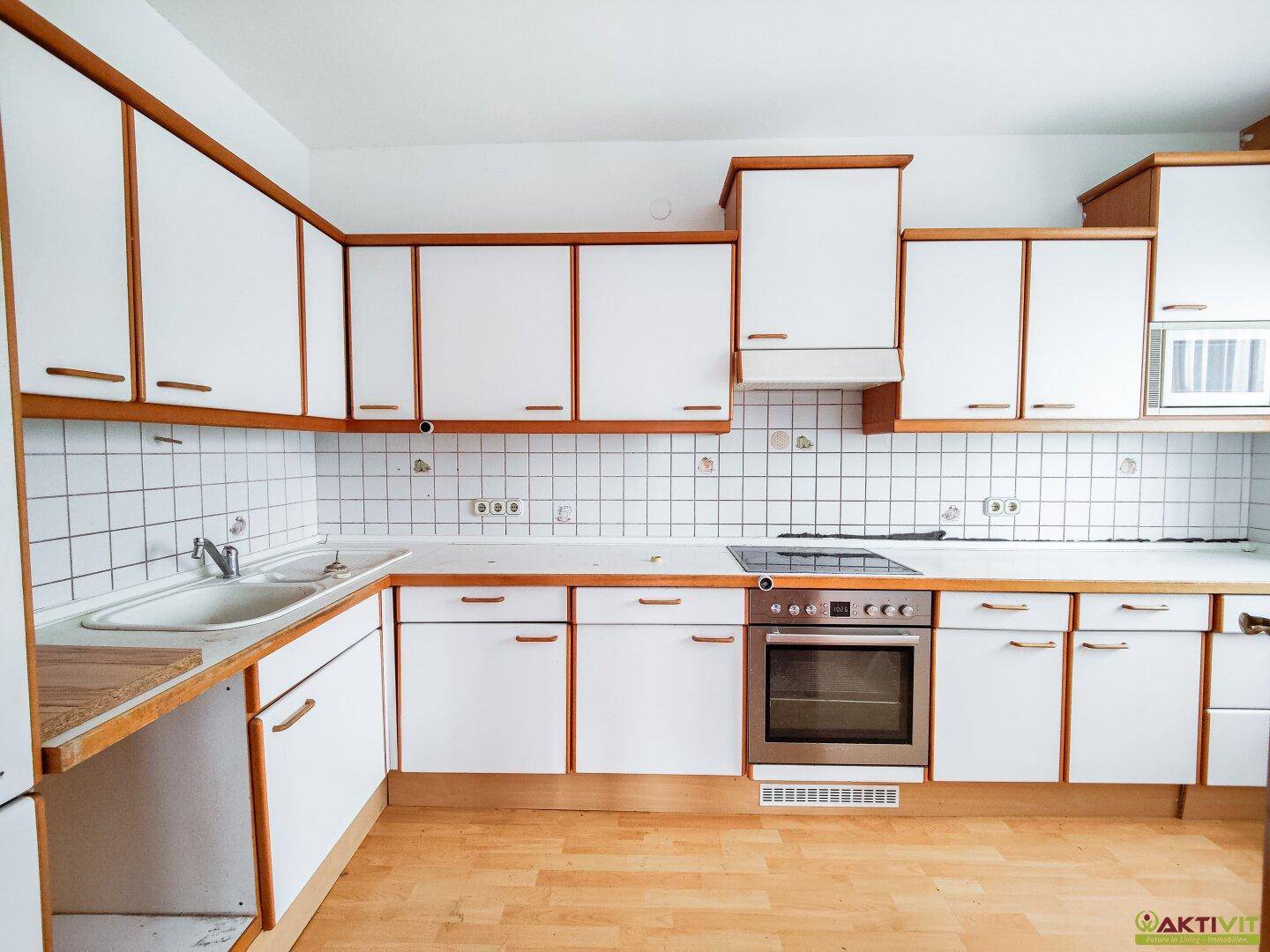 Leere Küche mit weißen Schränken, Fliesenrückwand und Herd.