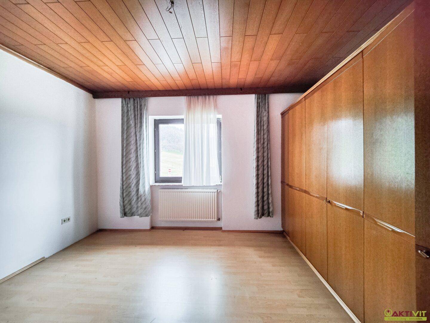 Schlafzimmer mit Holzdecke, Einbauschrank und Fenster mit Blick ins Grüne.