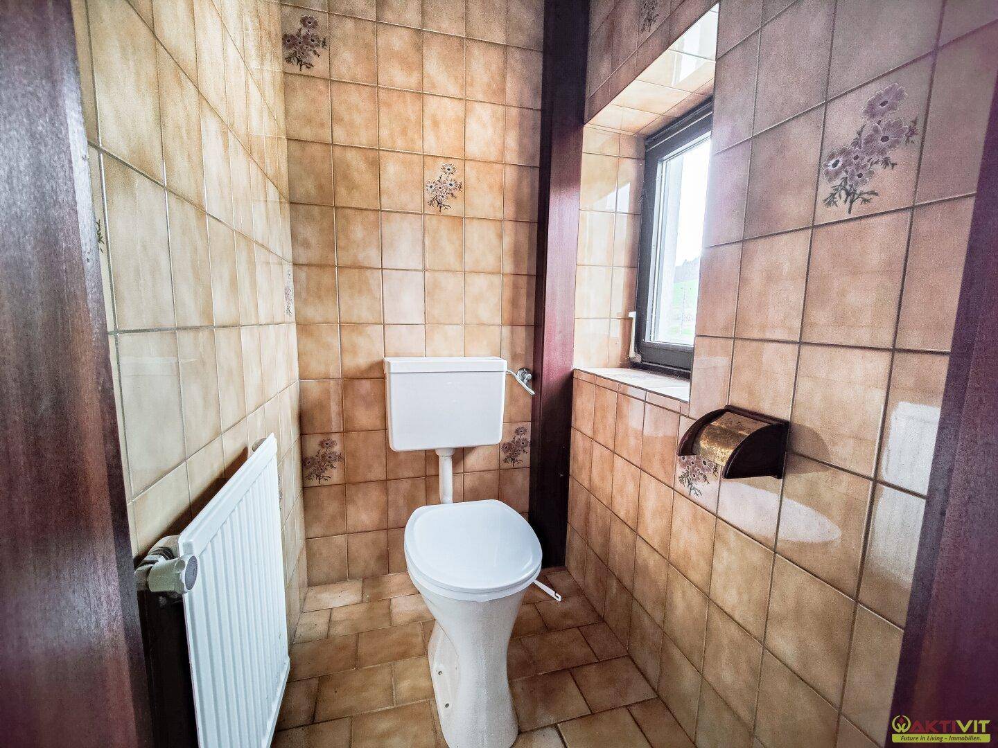 Kleines WC mit beigefarbenen Fliesen, Toilette und Fenster.