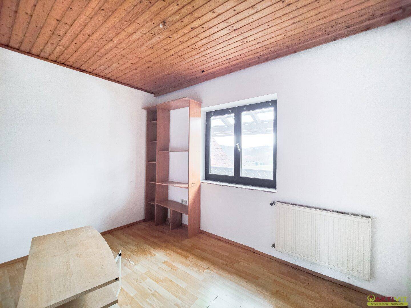 Helles Zimmer mit Holzdecke, Fenster und einfachem Regal.