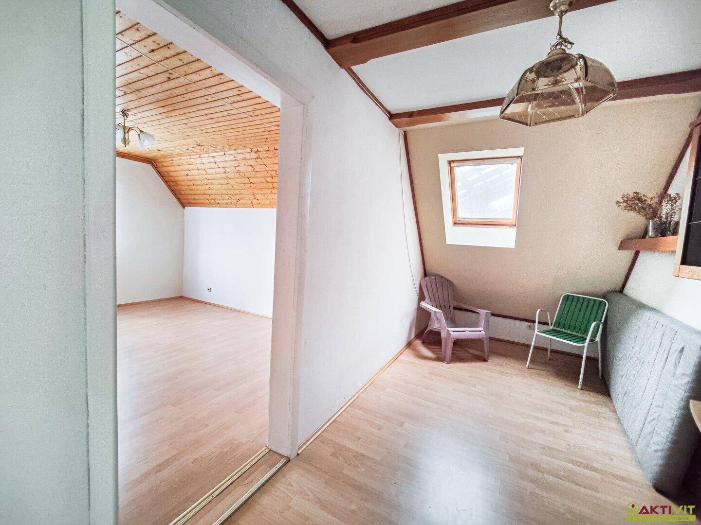 Dachgeschosszimmer mit schräger Decke und Holzverkleidung.