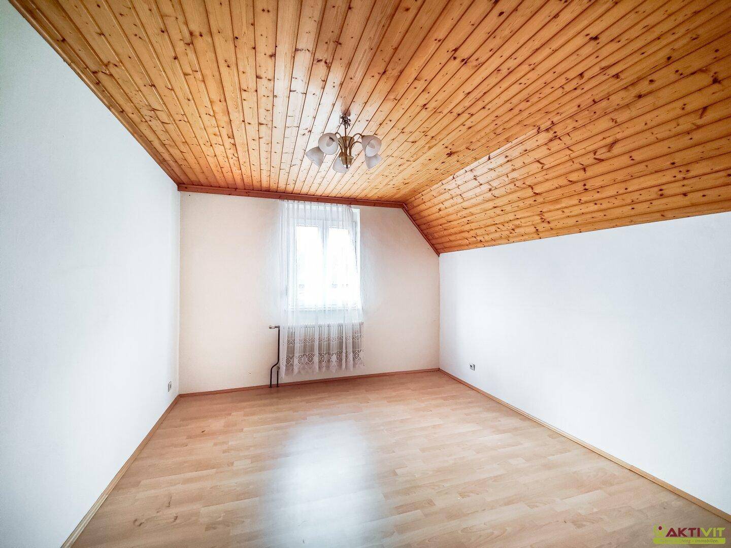 Helles Schlafzimmer im Dachgeschoss mit Holzdecke und Fenster.