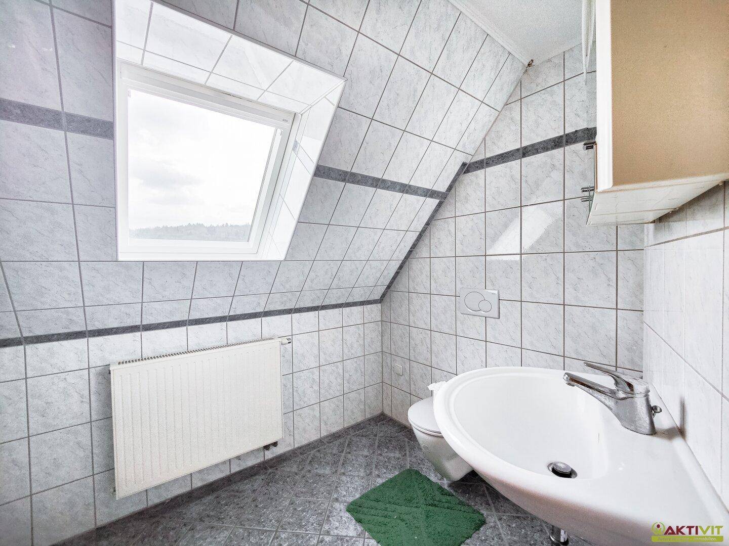 Badezimmer im Dachgeschoss mit Dachfenster, Waschbecken und grauen Fliesen.