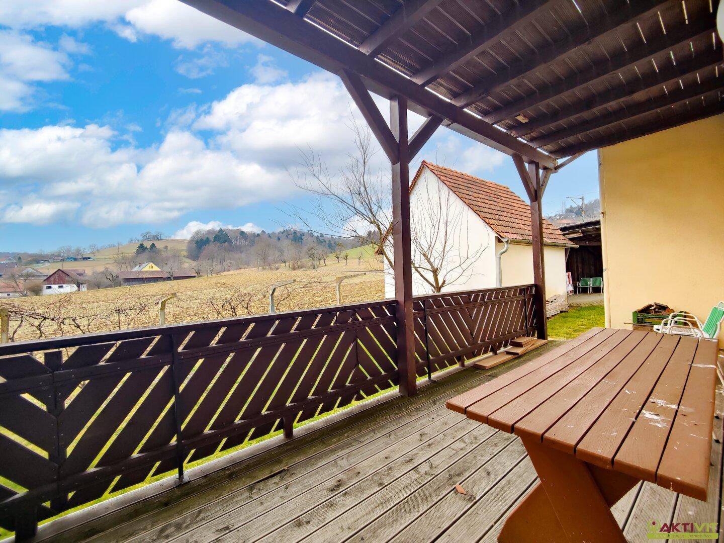 Überdachte Terrasse mit Holztisch und weitem Blick über die Landschaft.
