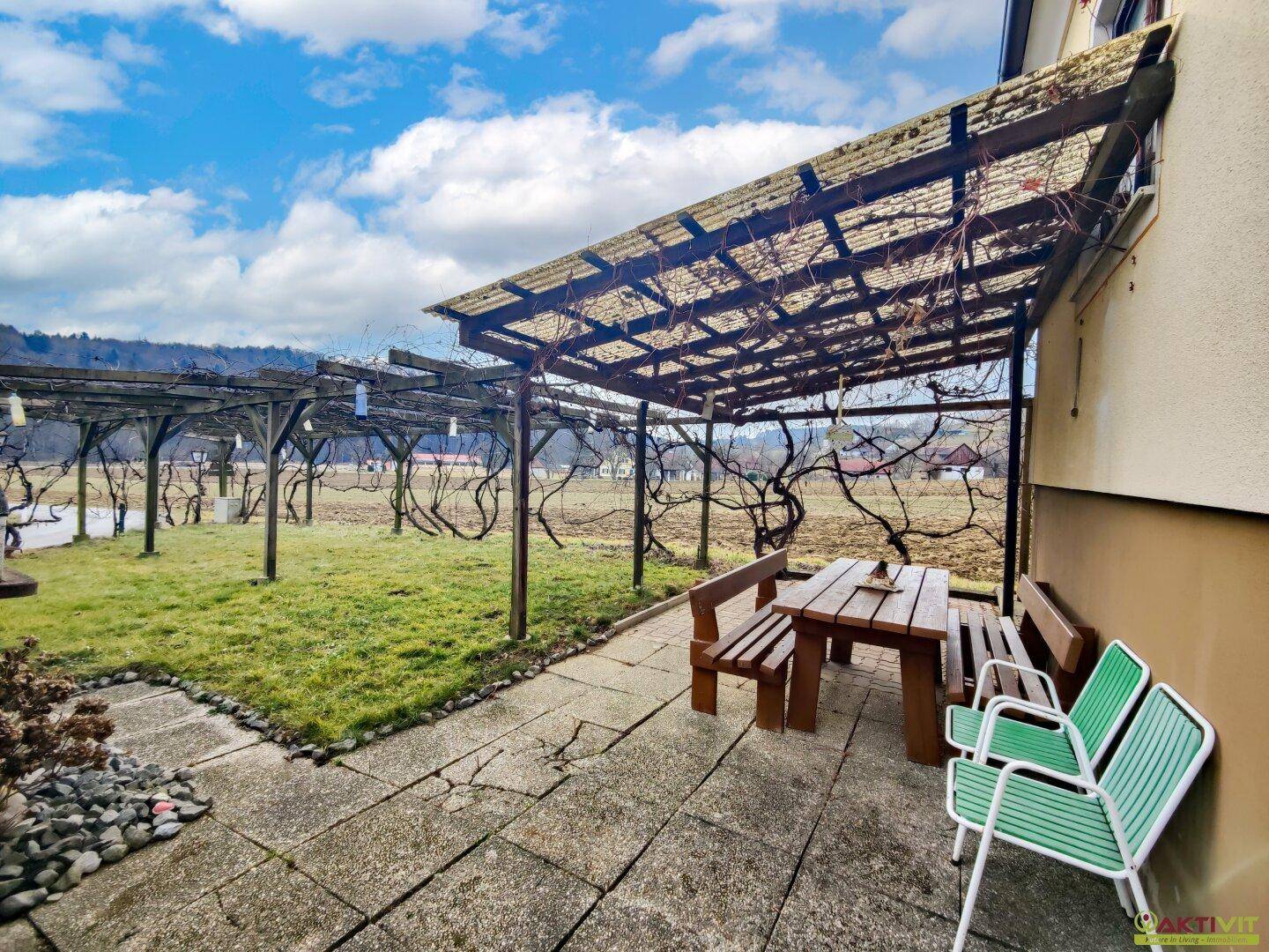 Gartenbereich mit gepflasterter Terrasse, Pergola und Sitzgelegenheiten.