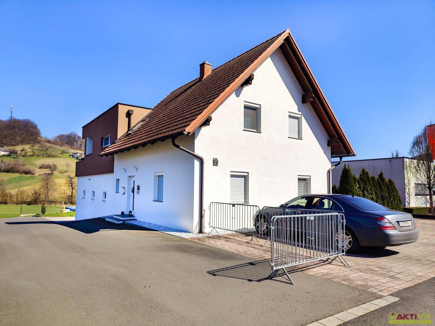 Seitenansicht des Hauses mit weißer Fassade, Satteldach und gepflasterter Einfahrt.