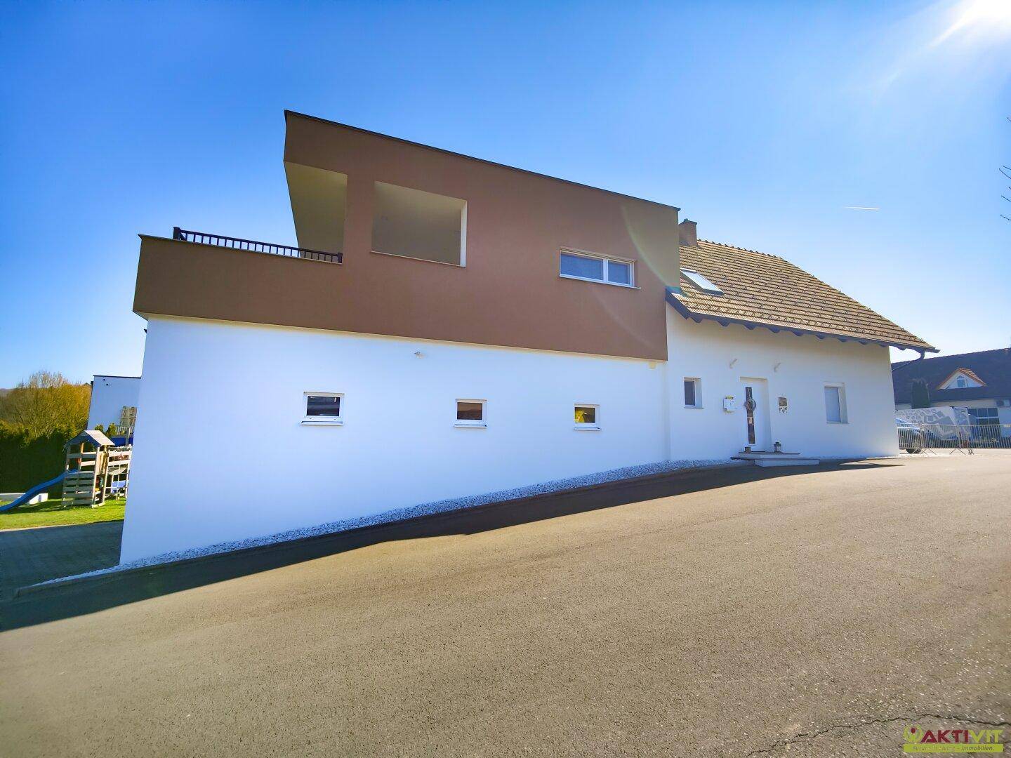 Moderne Architektur des Hauses mit weißer Fassade, braunem Anbau und einer oberen Terrasse.