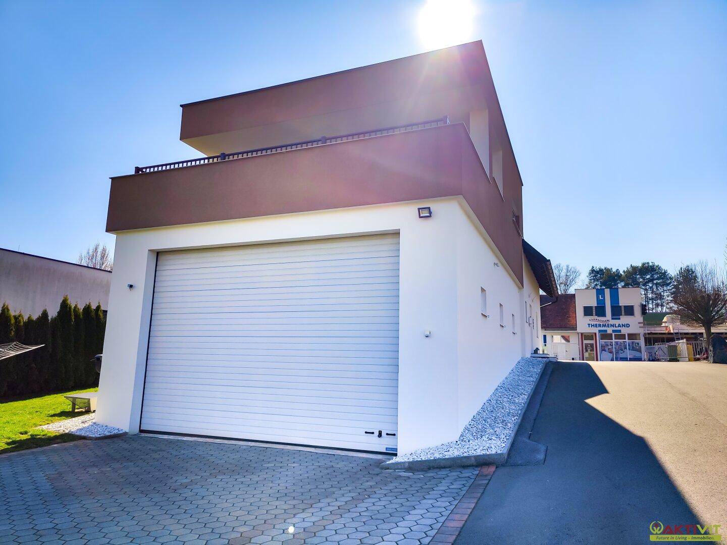Ansicht der modernen Garage mit Rolltor und der weißen Fassade des Gebäudes.