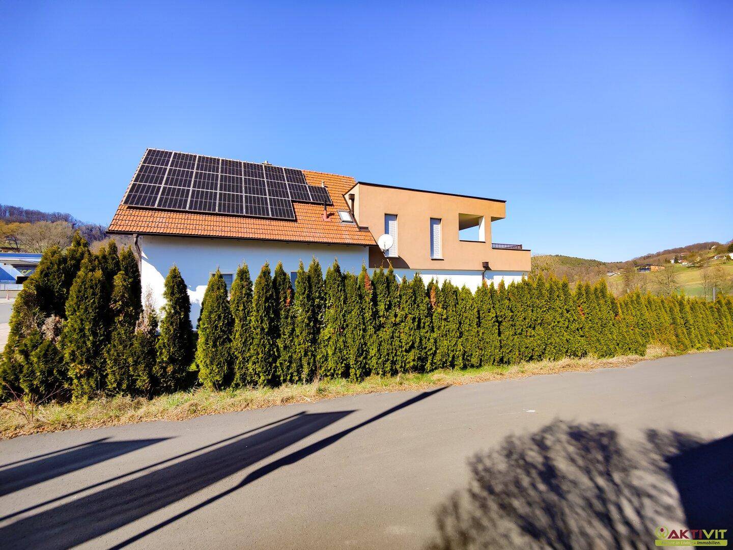 Rückansicht des Hauses mit Photovoltaikanlage auf dem Dach und einer hohen Hecke.