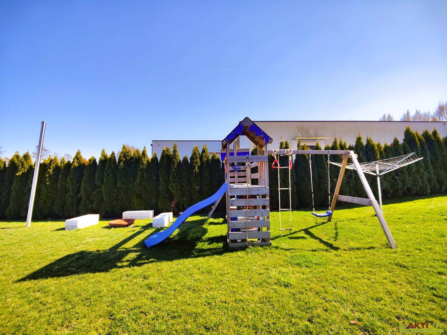 Großer Gartenbereich mit Kinderspielplatz, Rutsche und Schaukel vor einer hohen Hecke.