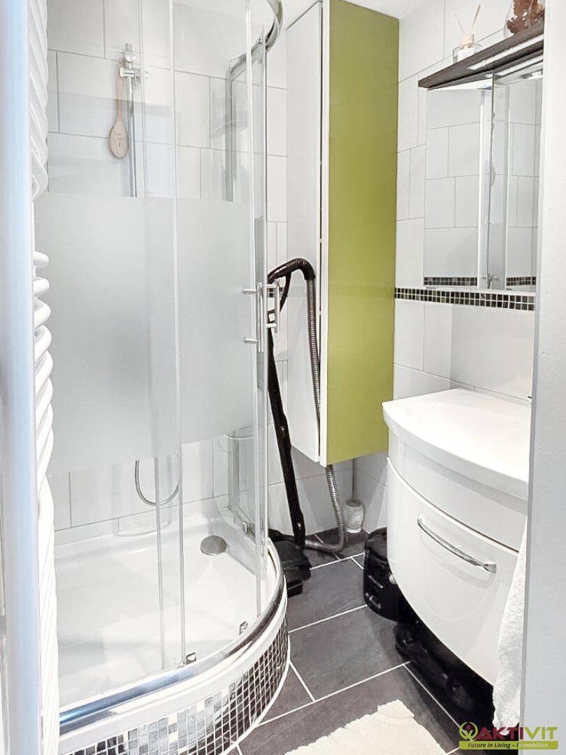 Modernes Badezimmer mit Duschkabine, Waschbecken und grünen Akzenten, ausgestattet mit Handtuchheizkörper.