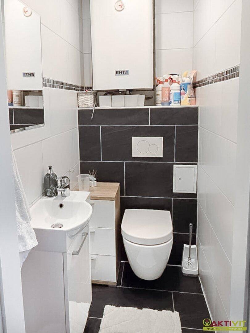 Separates WC mit wandhängender Toilette, kleinem Waschbecken und dunklen Bodenfliesen in modernem Design.