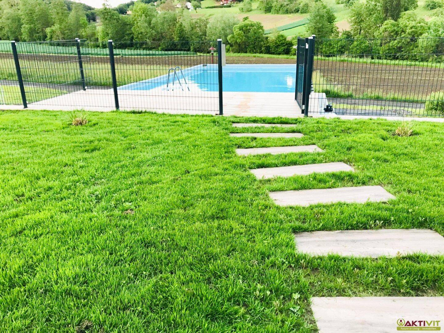 Gepflegter Rasenbereich mit Trittsteinen, die zum umzäunten Swimmingpool und zur ländlichen Umgebung führen.