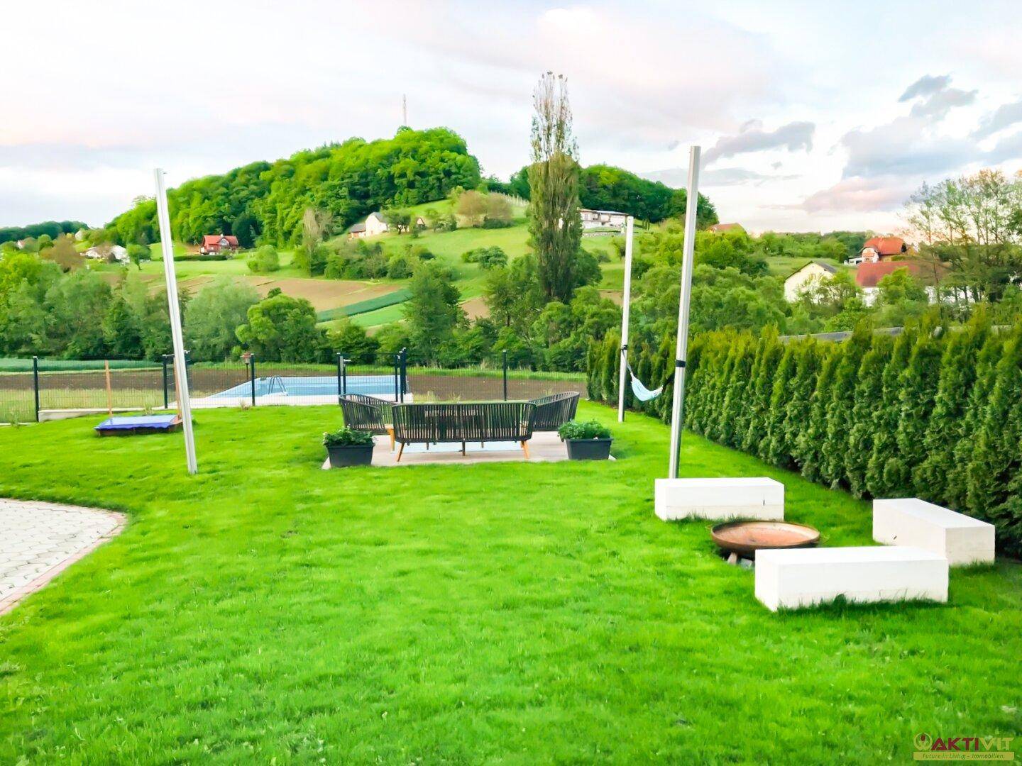 Großer Garten mit moderner Sitzgruppe, Feuerstelle und Blick auf die grüne Hügellandschaft mit Pool.