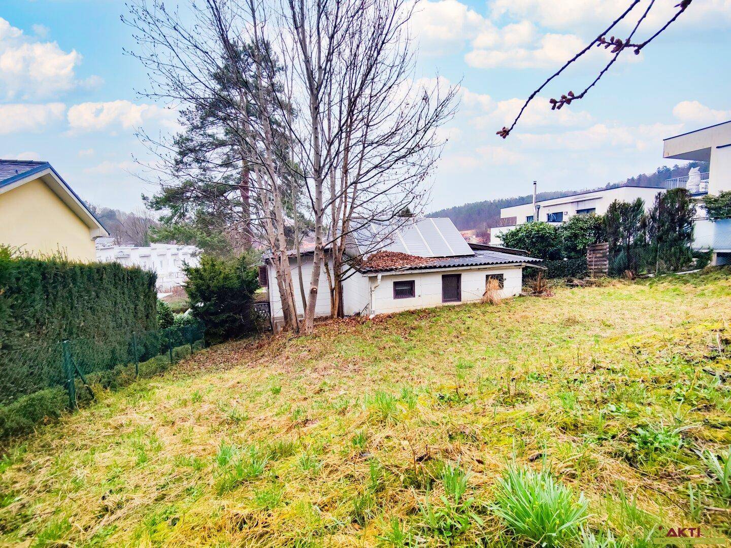 Kleines weißes Nebengebäude mit Photovoltaikanlage auf dem Dach, umgeben von einer grünen Wiese.