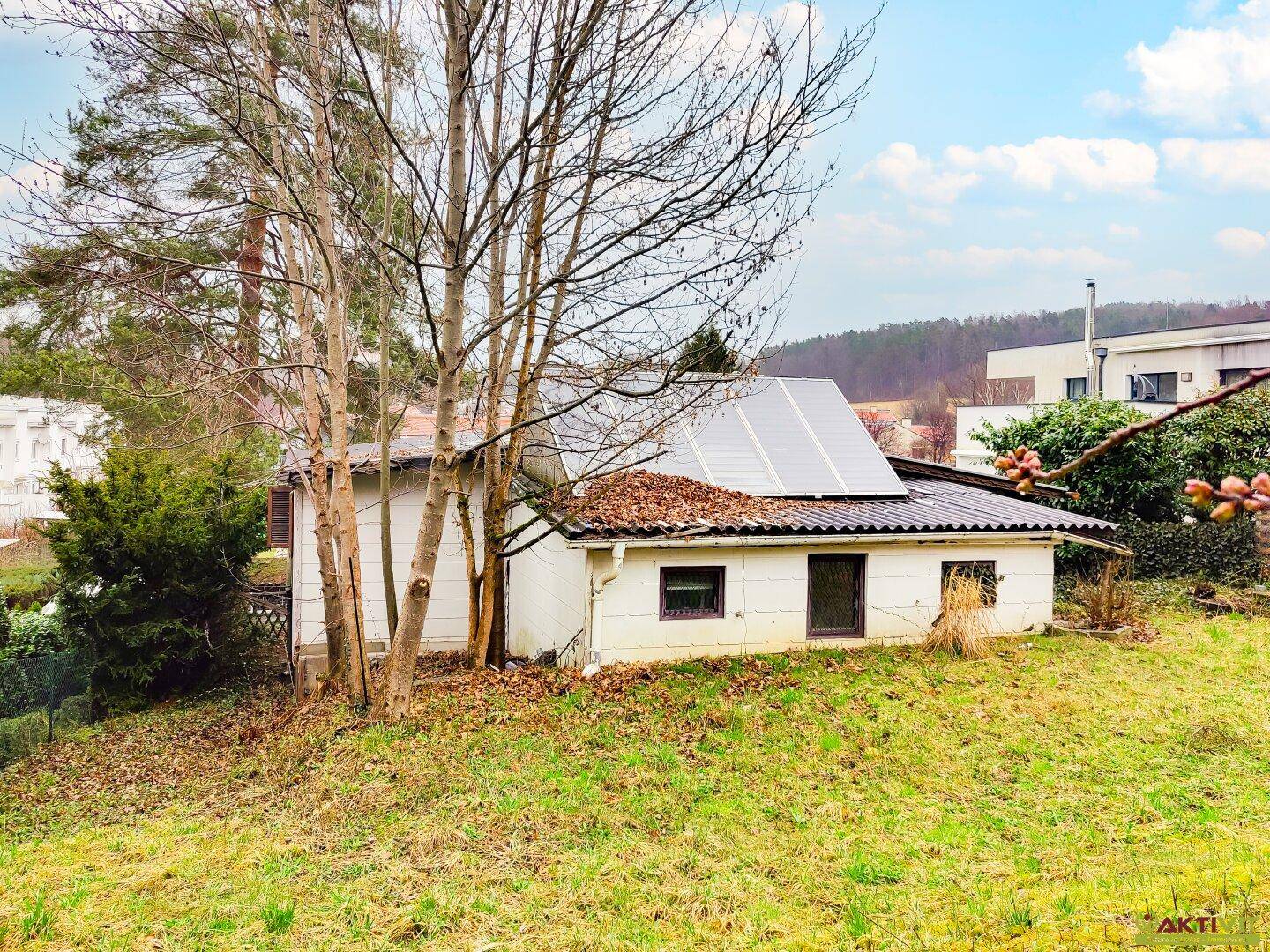 Nahaufnahme des Nebengebäudes mit Photovoltaikmodulen auf dem Dach und umgebender Natur.