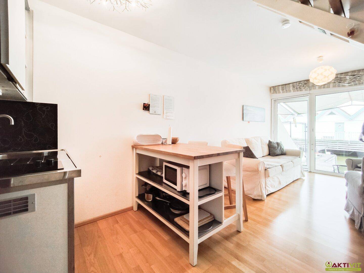 Kompakte Küchenzeile und Wohnbereich mit Holzboden und Zugang zur Terrasse.