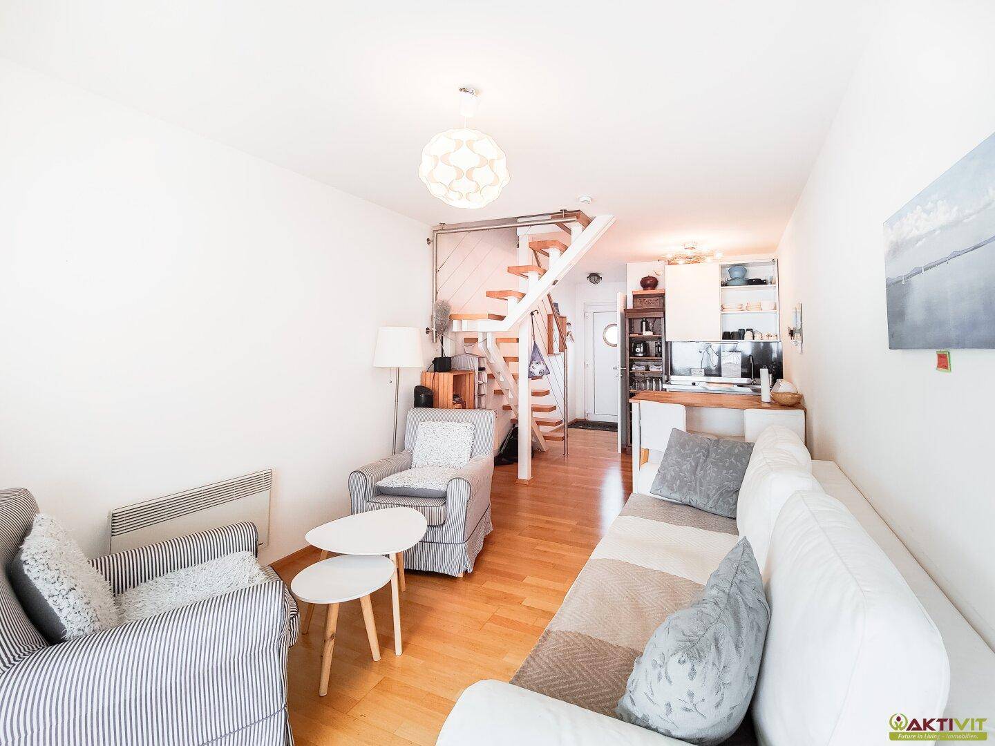 Heller Wohnbereich mit offener Treppe, Sofa und Blick auf die integrierte Küchenzeile.