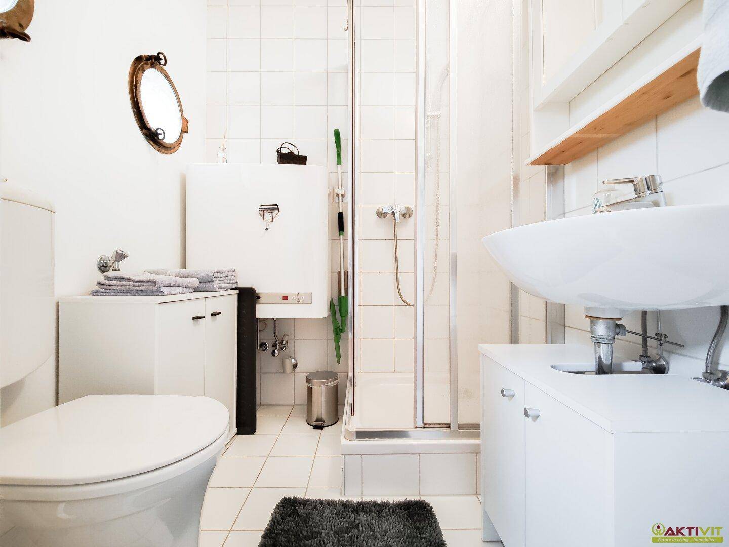 Modernes Badezimmer mit Dusche, WC und Waschbecken in hellen Fliesen.