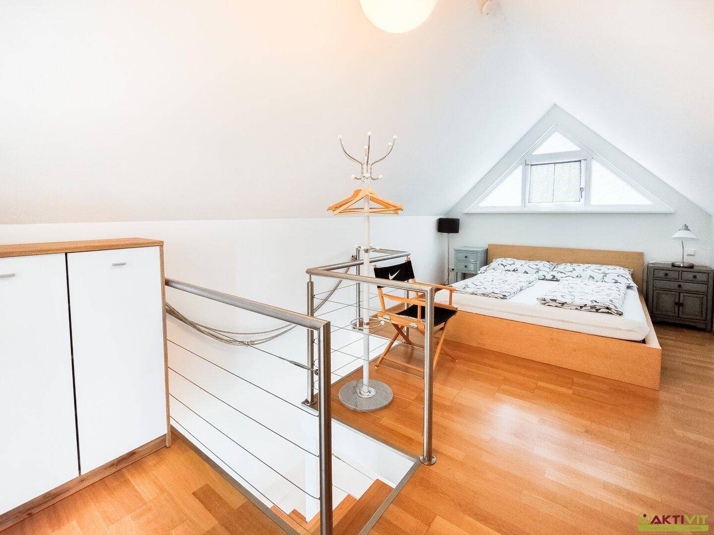 Offenes Schlafzimmer im Dachgeschoss mit Holzboden und dreieckigem Fenster.