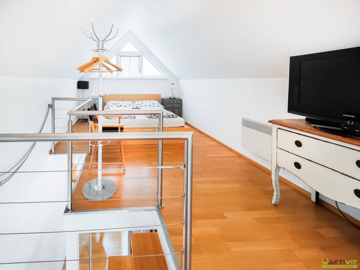 Schlafbereich im Dachgeschoss mit Holzboden, TV und Blick auf die Treppe.