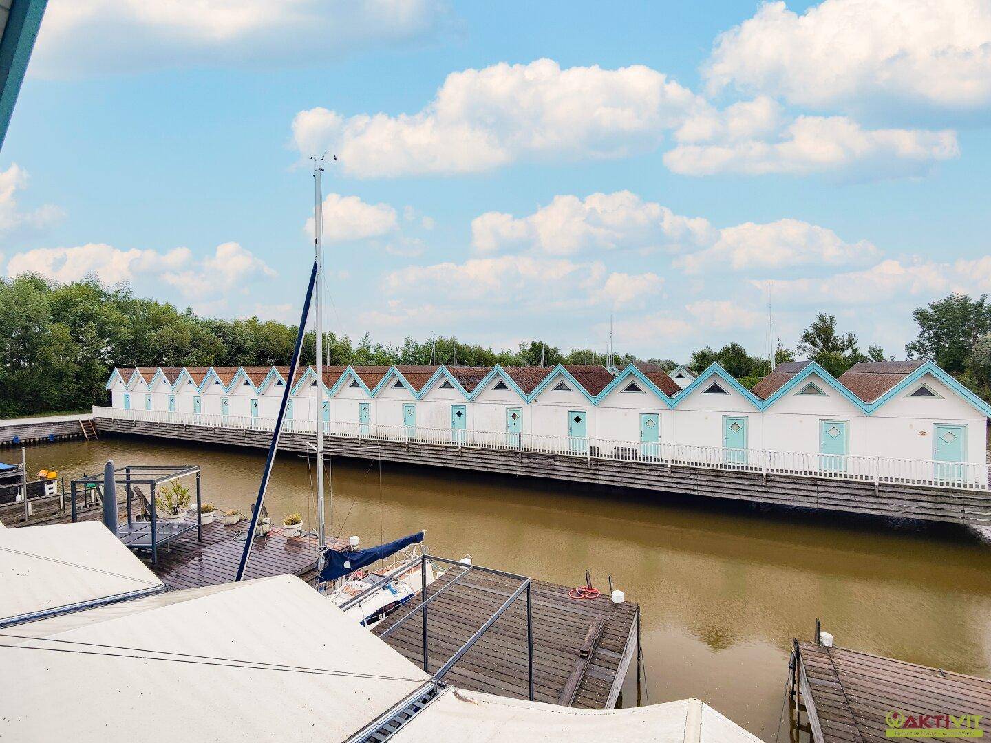 Eine Reihe von Ferienhäusern am Kanal mit Bootsanlegestellen unter blauem Himmel.