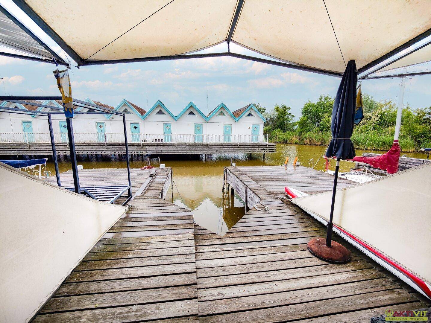 Weitläufige Holzterrasse mit Sonnenschirm und direktem Zugang zum Wasser.
