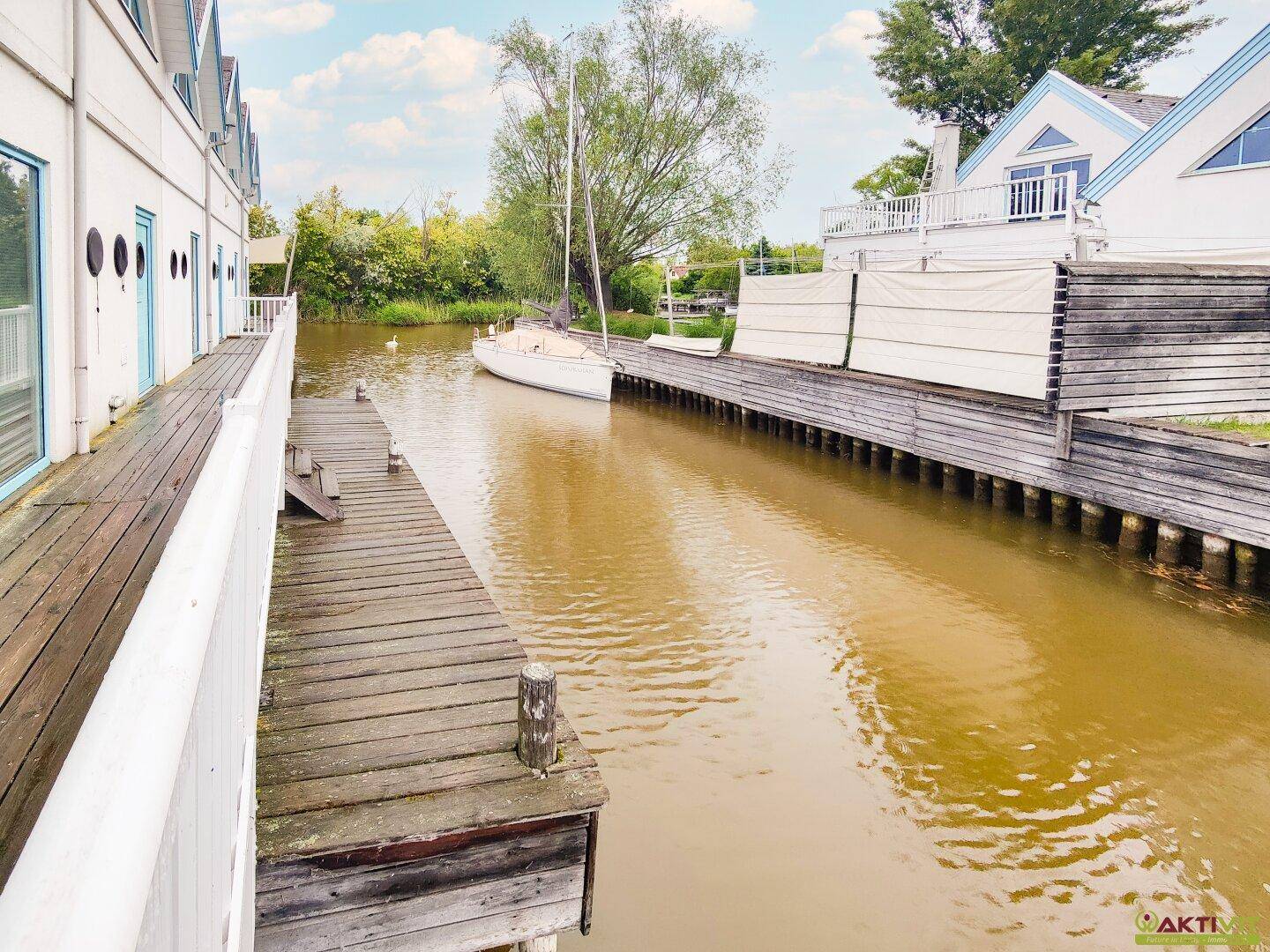 Ruhiger Kanalabschnitt mit einem Segelboot und den Ferienhäusern am Ufer.