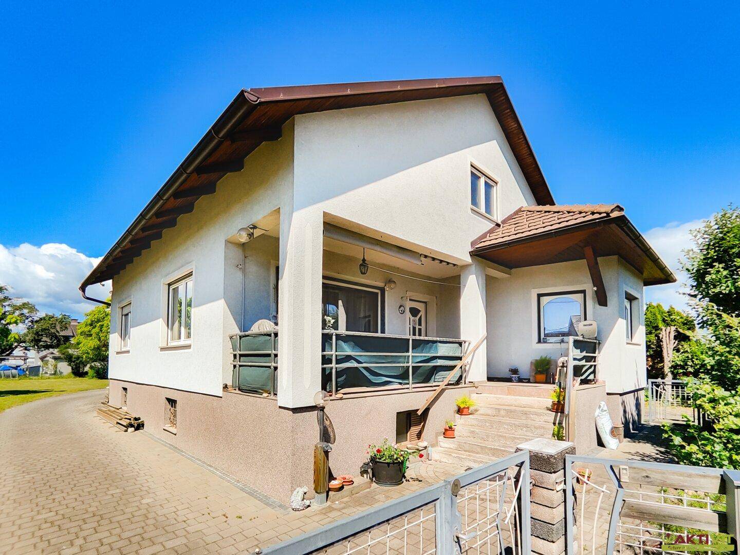 Seitenansicht des Hauses mit Balkon und Treppe, umgeben von Grünflächen und Bäumen.