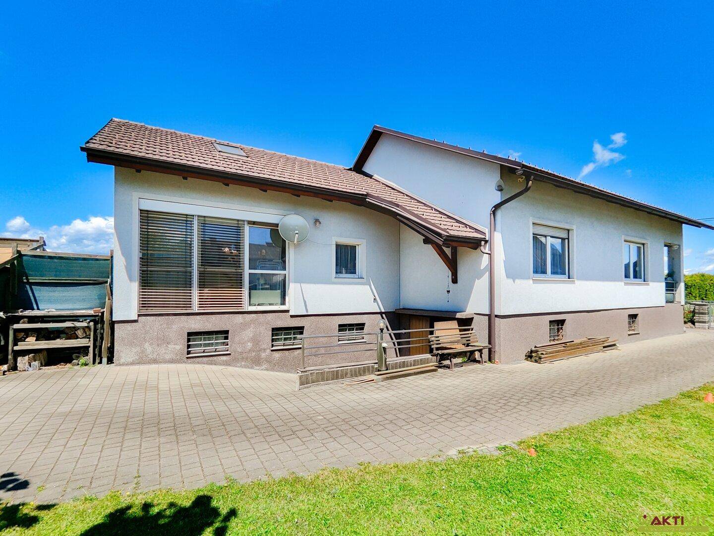 Ansicht des Hauses von außen mit gepflasterter Auffahrt und Rasenfläche unter blauem Himmel.
