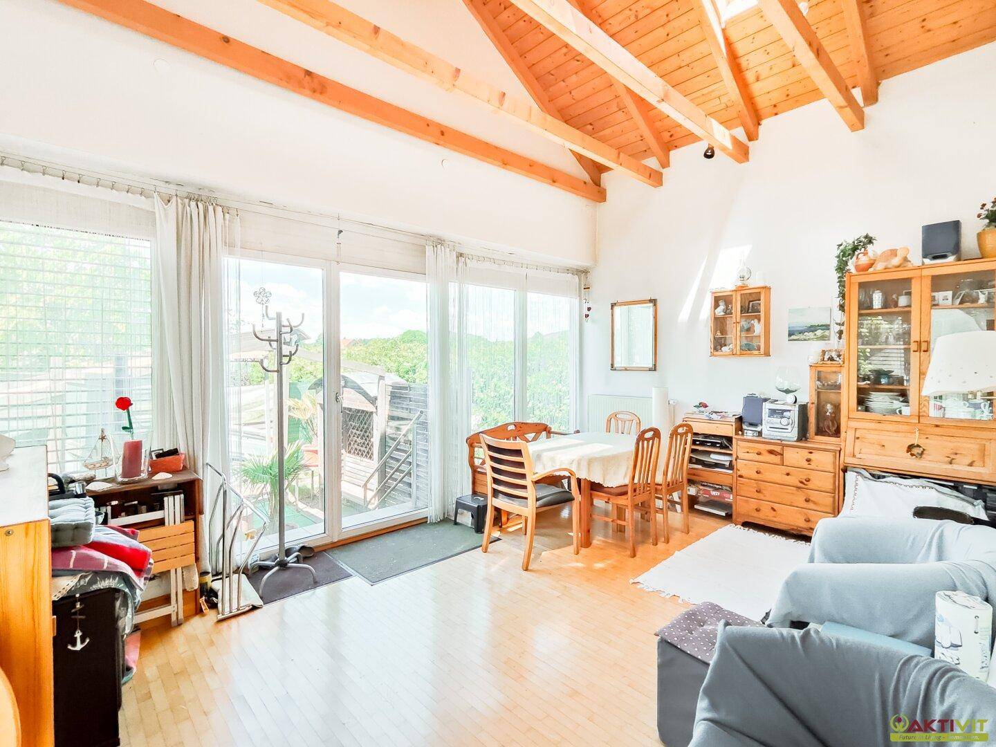 Geräumiger Wohn- und Essbereich mit Holzbalkendecke, großen Fenstern und Zugang zur Terrasse.