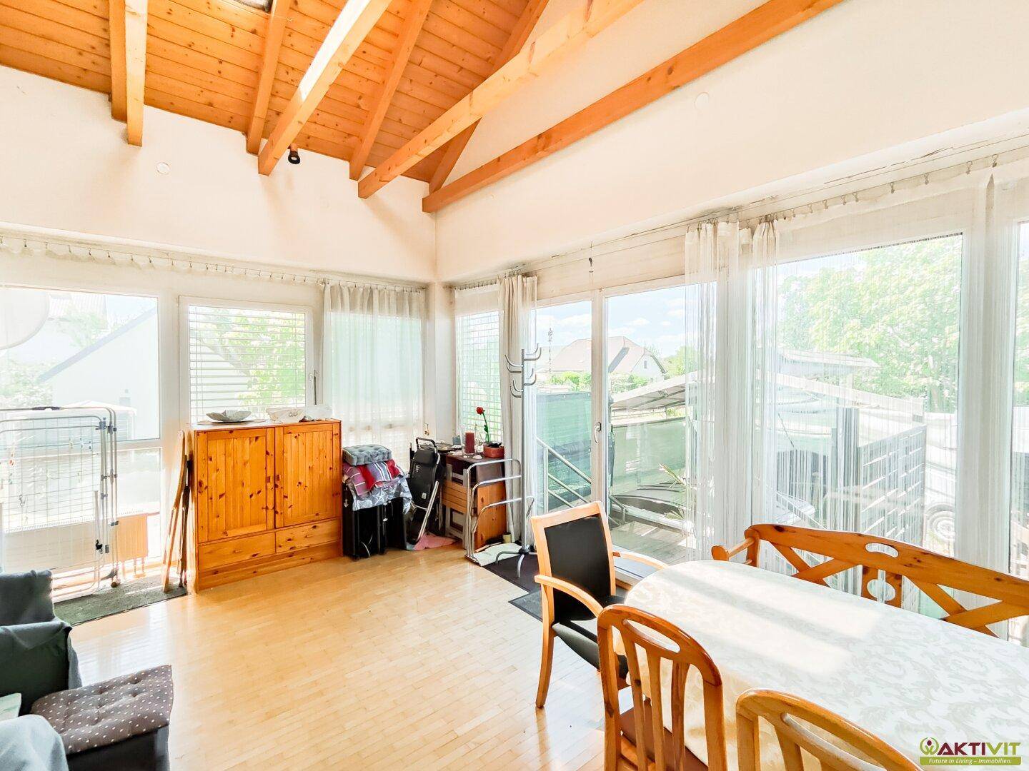 Heller Wohnbereich mit großen Fenstern, Holzboden und viel Tageslicht, ideal für Familienleben.