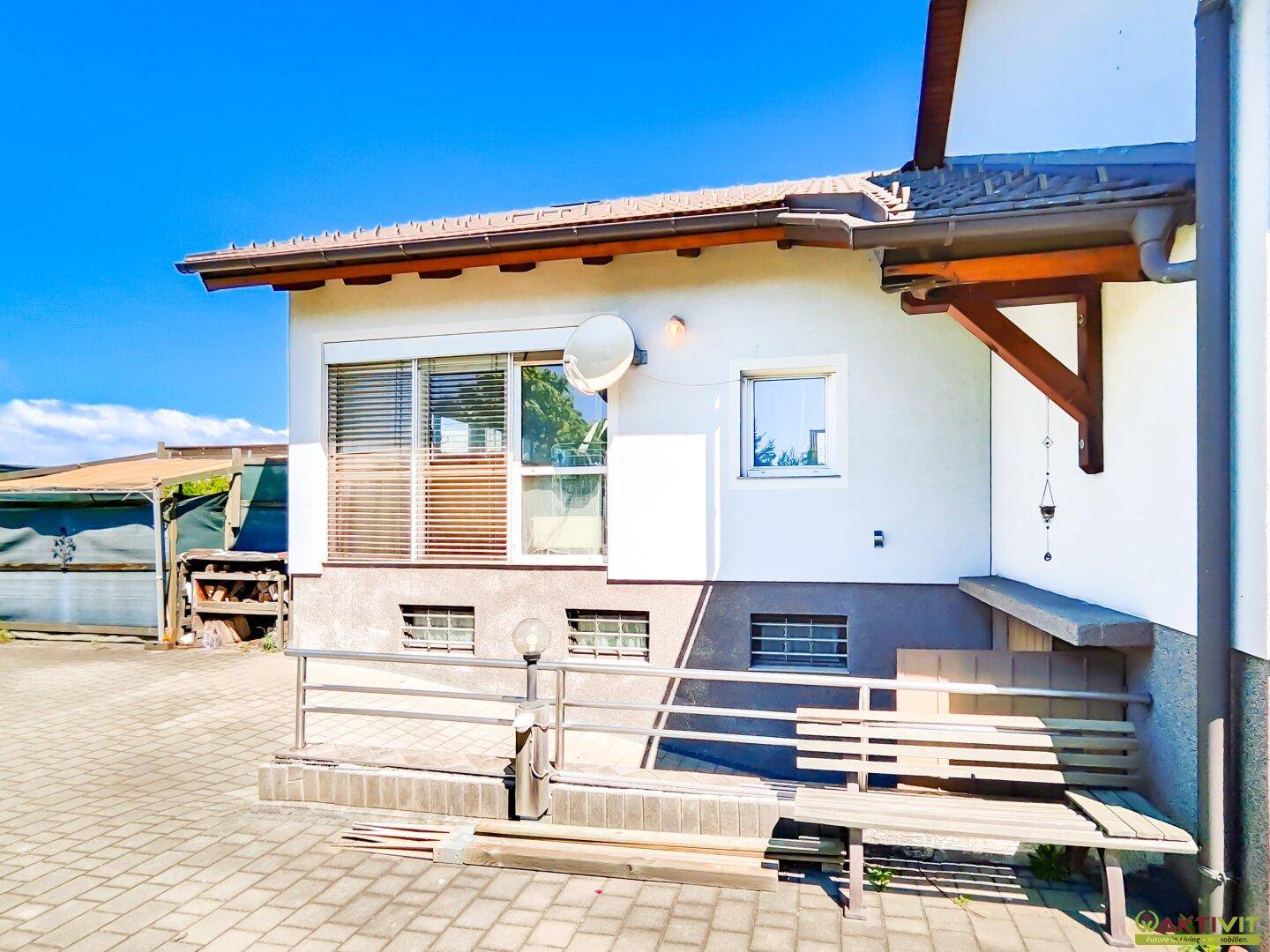Ansicht des Hauses von der Seite mit einer kleinen Sitzbank und gepflastertem Bereich.
