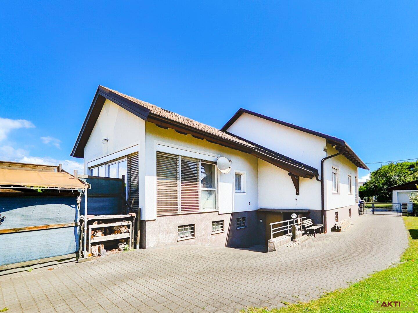 Seitenansicht des Hauses mit gepflasterter Auffahrt und Nebengebäuden unter blauem Himmel.