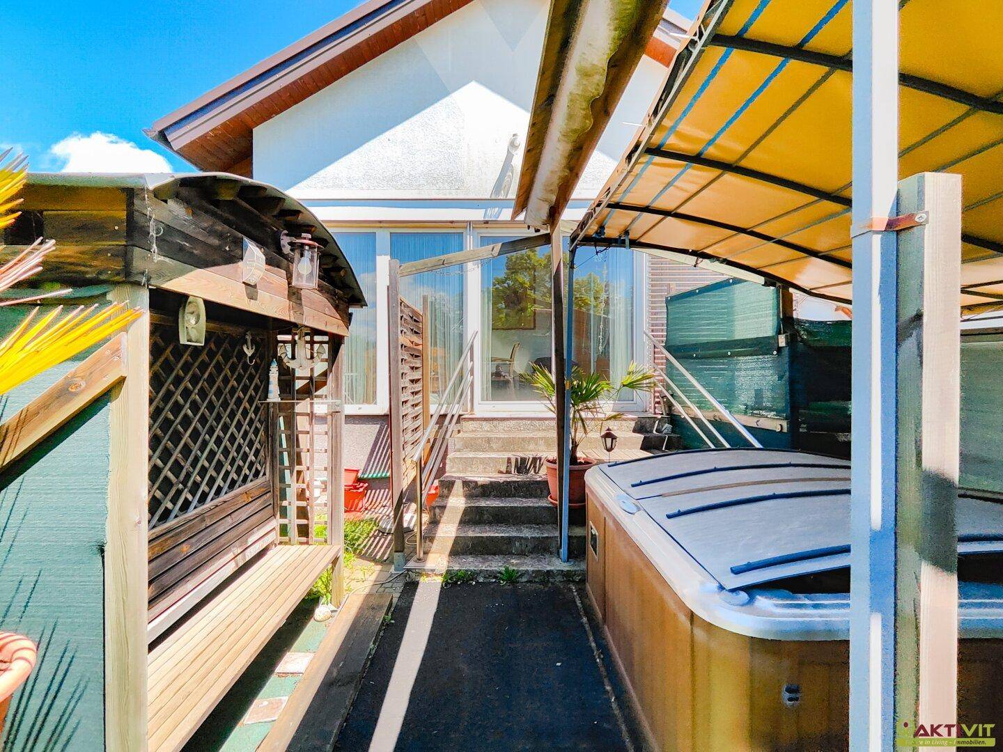 Überdachter Außenbereich mit Whirlpool und Zugang zu einem verglasten Anbau des Hauses.