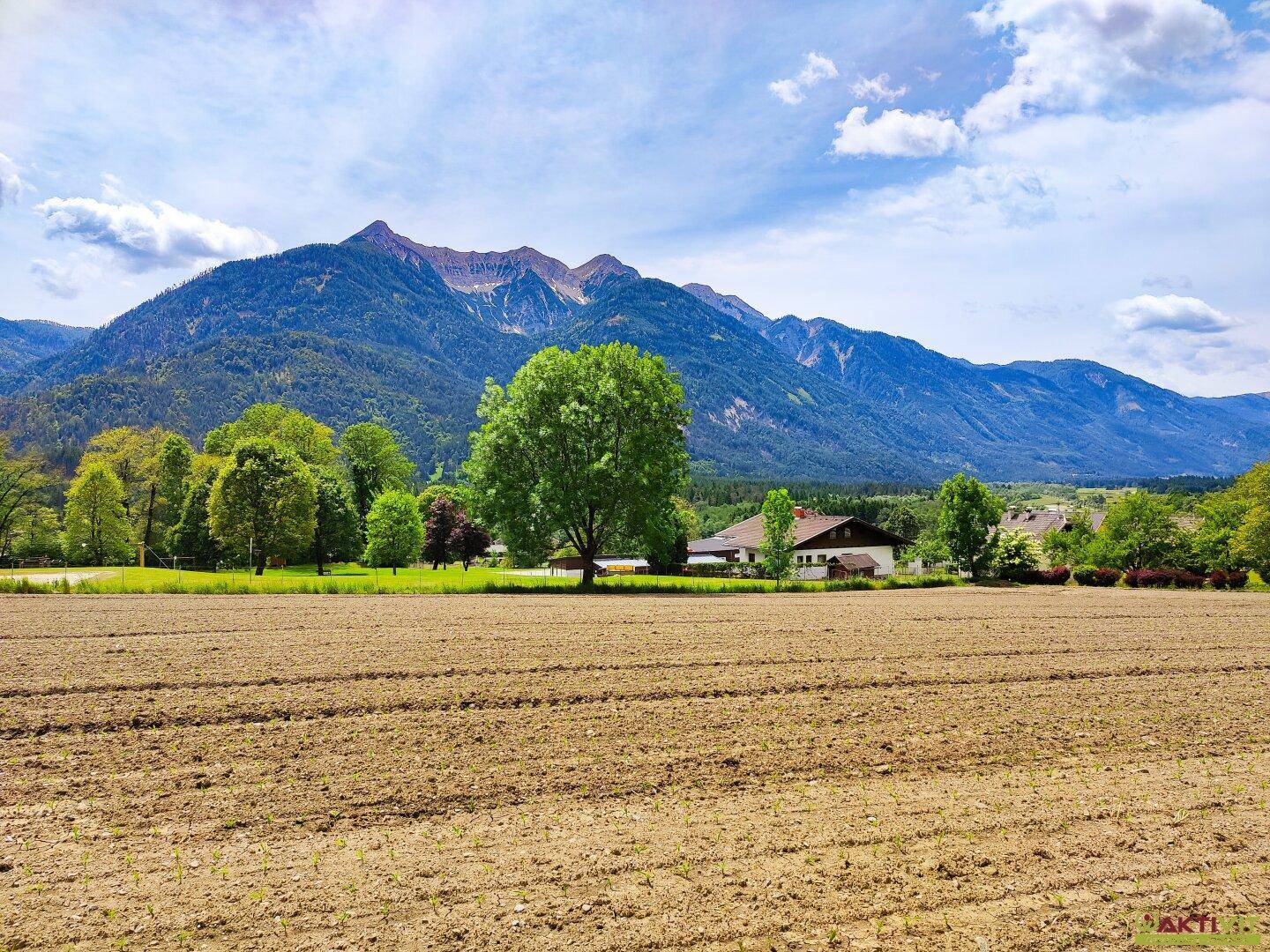 Ackerfläche mit vereinzelten Häusern und einer beeindruckenden Bergkette am Horizont.