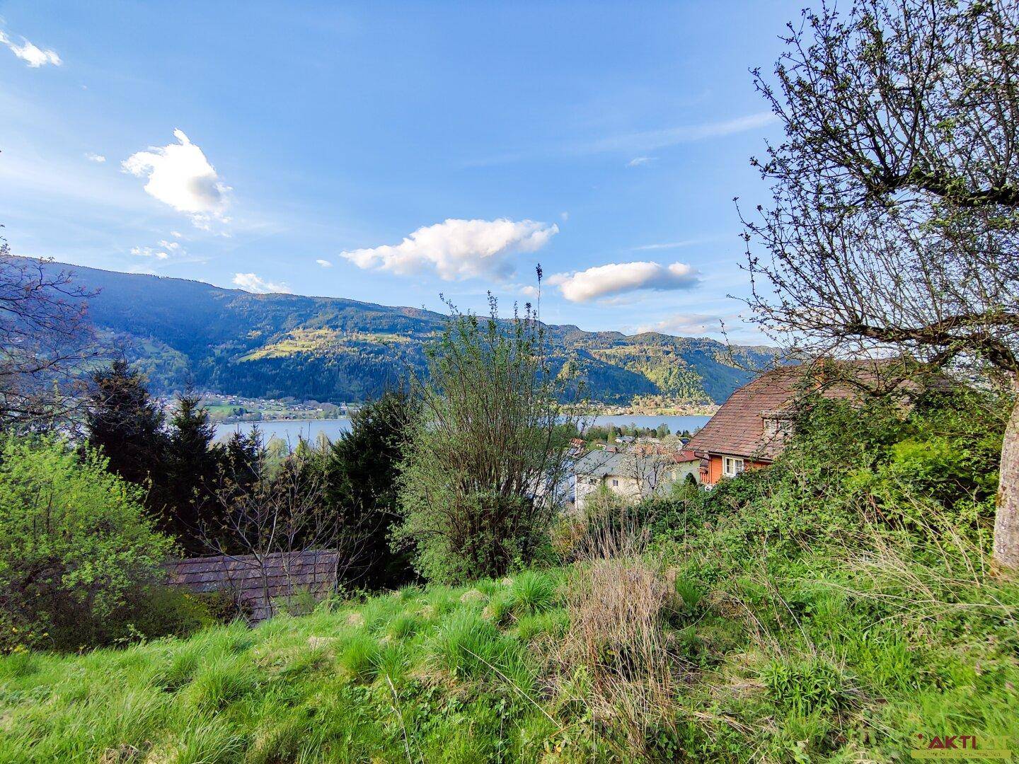 Malerischer Ausblick auf den See und die umliegenden Berge mit einem Teil eines Hauses im Vordergrund.